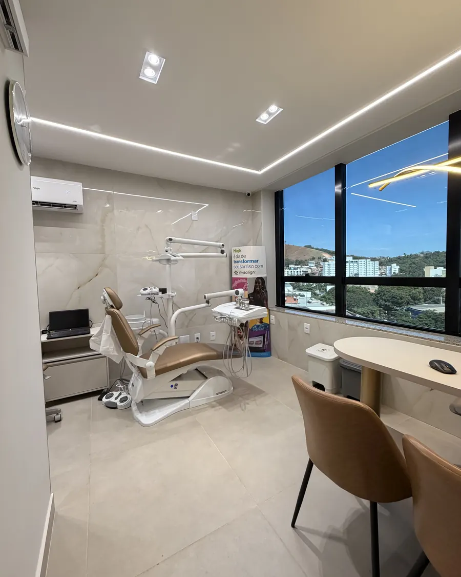 Consultório iluminado pela luz do dia, com a cadeira odontológica de frente para a janela.