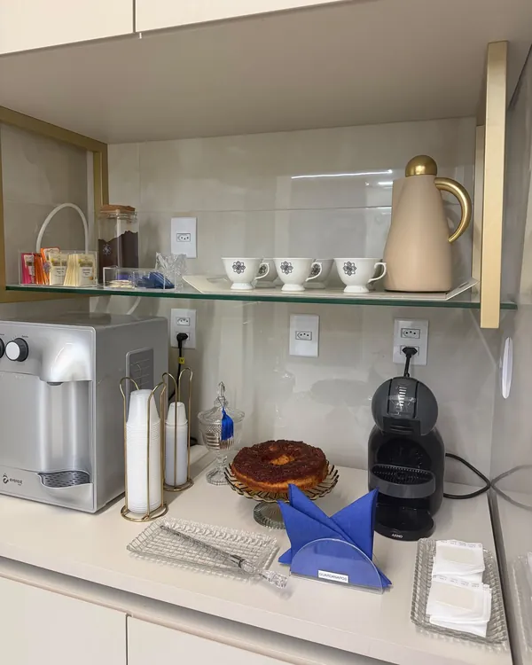 Cantinho do café, com cafeteira, xícaras, água e um bolo para os pacientes.