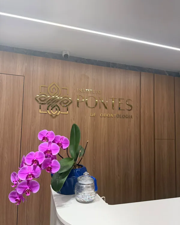 Recepção do Instituto, com uma orquídea no balcão e o logotipo dourado na parede de madeira.